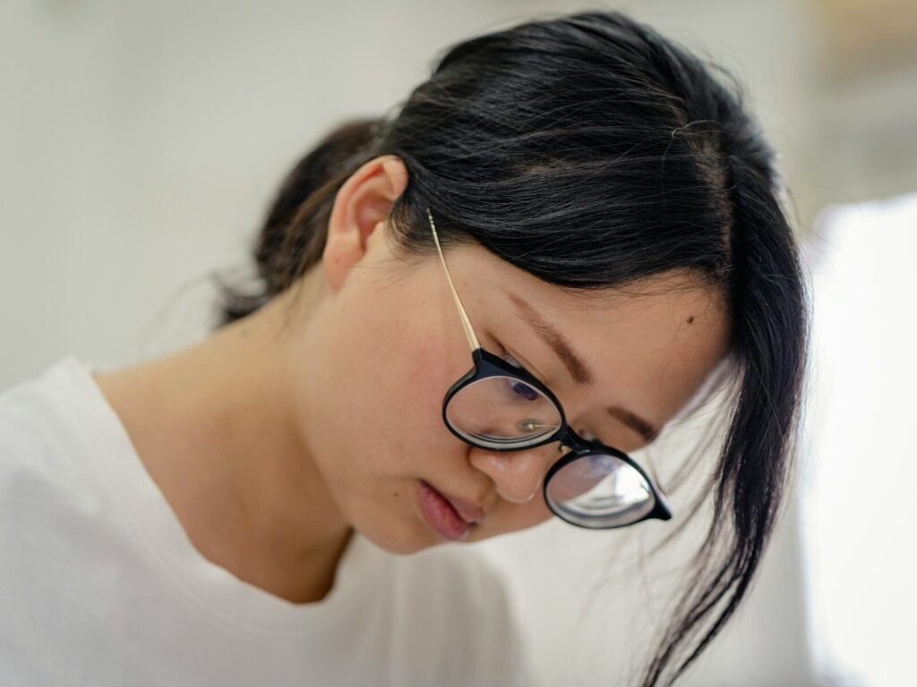 Woman wearing glasses looking down at a screen with tired eyes, illustrating digital eye strain from long hours at a monitor